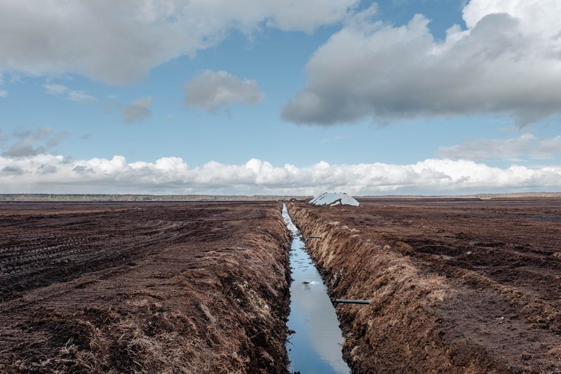A desolate extraction site. The blue sky is reflected in a large drainage ditch filled with water from the surrounding peatland.